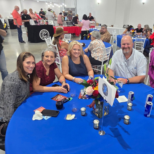 Guests smiling at a blue table during Taste of Milam, a community fundraiser supporting CASA of Milam County.