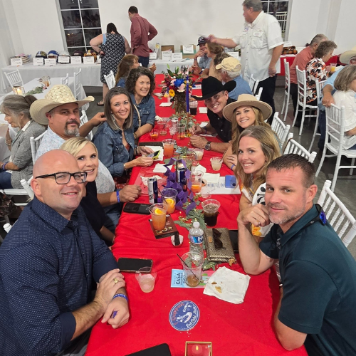 A group of community supporters smiling around a decorated table at Taste of Milam.