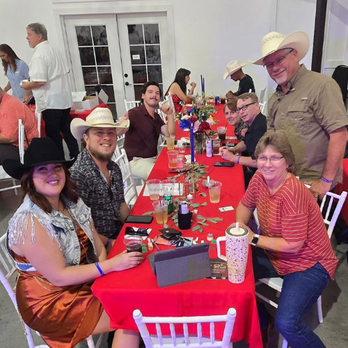 Guests smiling at a decorated table during Taste of Milam, an annual CASA of Milam County fundraiser.