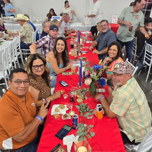 A group of community supporters smiling around a decorated table at Taste of Milam to support Milam County CASA